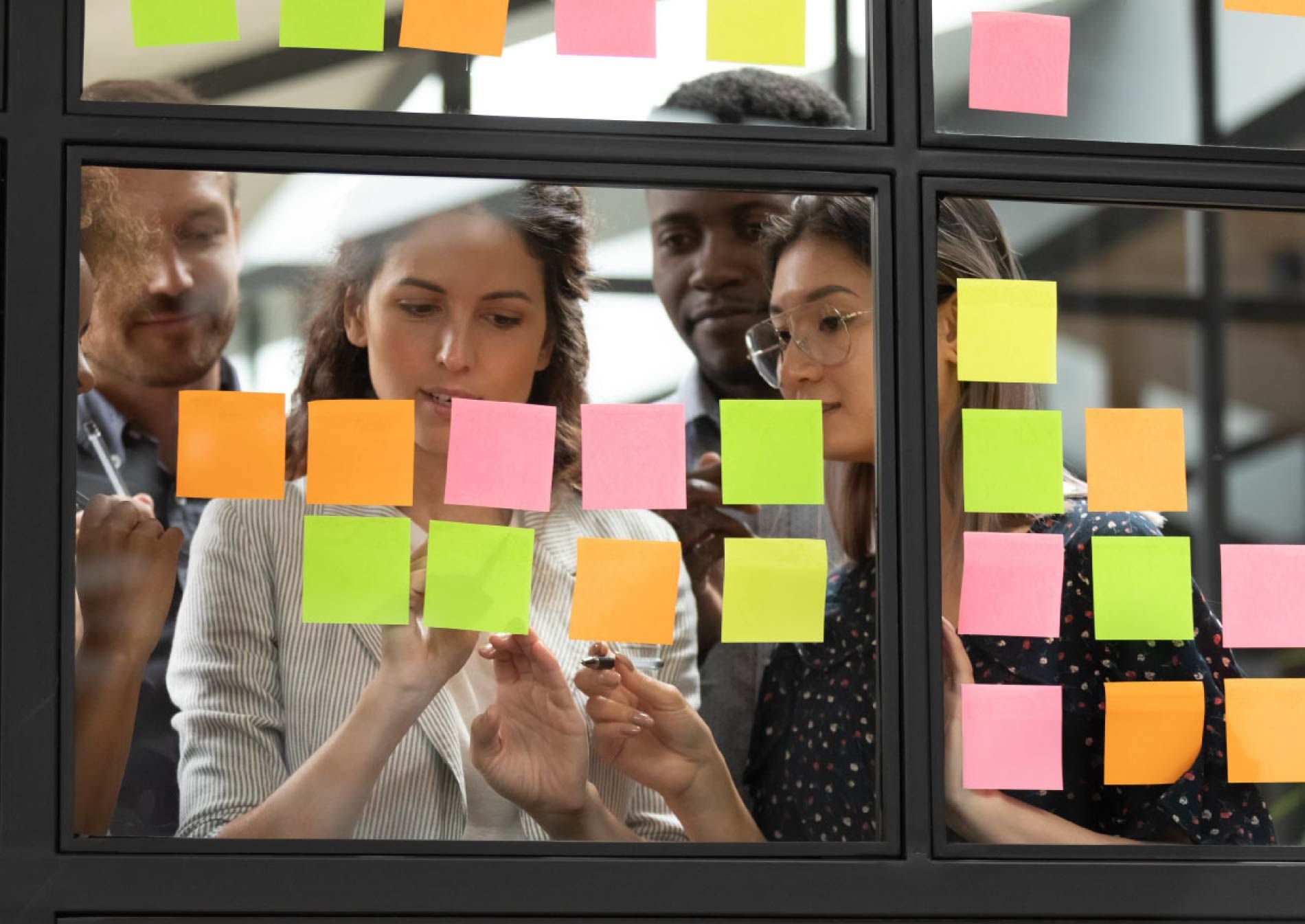 Artificial Intelligence in Scaled Agile. Vooraanzicht van een Agile team staand voor een raampartij in een kantoorruimte. De ruiten zijn volgeplakt met gekleurde post-its. De jonge teamleden kijken naar de post-its die onderdeel zijn van het kanban-organisatieproces. Artificial Intelligence in Scaled Agile. Vooraanzicht van een Agile team staand voor een raampartij in een kantoorruimte. De ruiten zijn volgeplakt met gekleurde post-its. De jonge teamleden kijken naar de post-its die onderdeel zijn van het kanban-organisatieproces. Artificial Intelligence in Scaled Agile. Vooraanzicht van een Agile team staand voor een raampartij in een kantoorruimte. De ruiten zijn volgeplakt met gekleurde post-its. De jonge teamleden kijken naar de post-its die onderdeel zijn van het kanban-organisatieproces. Artificial Intelligence in Scaled Agile. Vooraanzicht van een Agile team staand voor een raampartij in een kantoorruimte. De ruiten zijn volgeplakt met gekleurde post-its. De jonge teamleden kijken naar de post-its die onderdeel zijn van het kanban-organisatieproces.